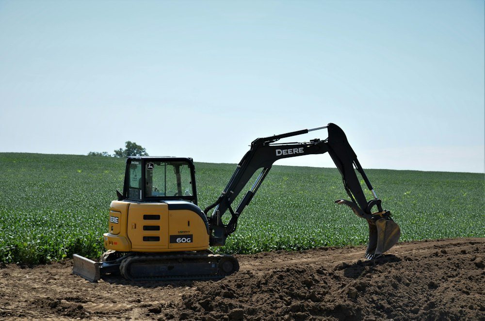 A mini excavator pulling stumps and brush on a partly cleared wooded lot